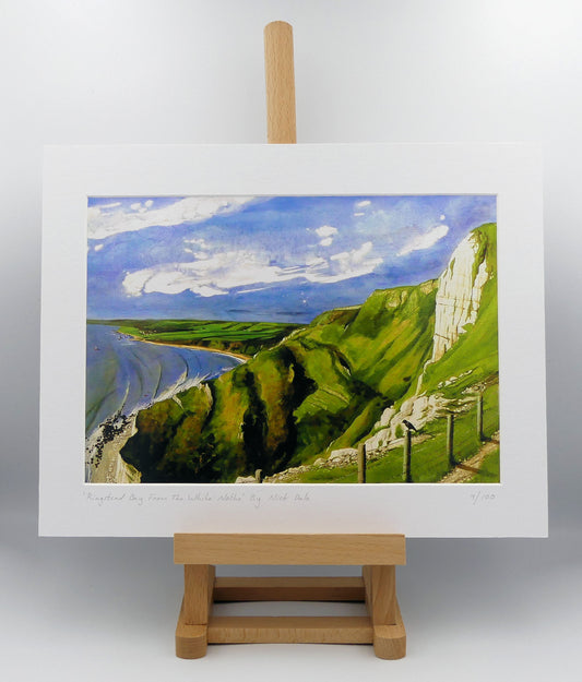 Image of a Medium Art Print featuring a copy of the painting 'Ringstead Bay From The White Nothe' by Nick Dale. The print depicts a view along the Jurassic Coast from the White Nothe chalk headland east of Ringstead Bay. The view looks west over the bay to the village of Ringstead & beyond. The print is situated on a small easel.