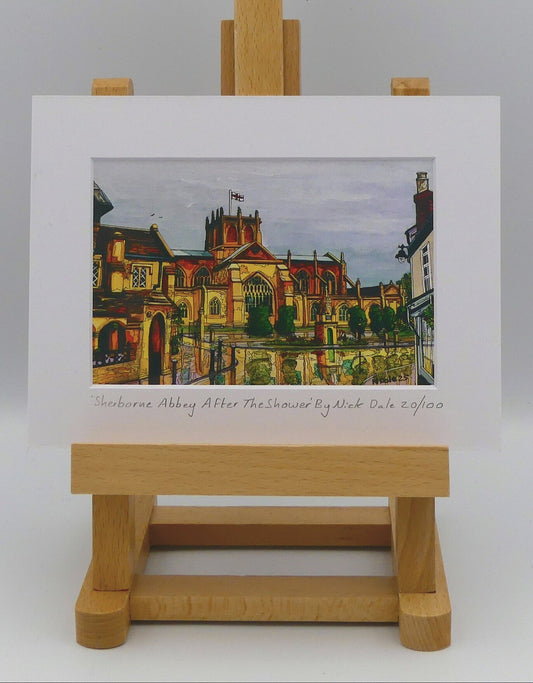 Image of Small Art Print featuring a copy of the painting 'Sherborne Abbey After The Shower' by Nick Dale. The print depicts a view of Sherborne Abbey (also known as the Abbey Church of St. Mary the Virgin), in Sherborne, Dorset. On the left hand side can be seen St Johns' Almshouse. The print is situated on a small easel.