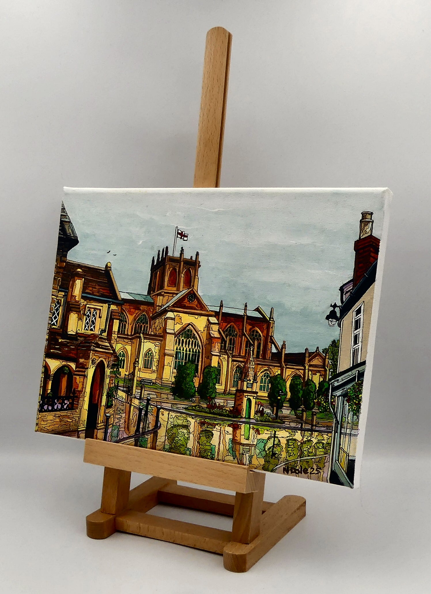 Image of the original painting 'Sherborne Abbey After The Shower' by Nick Dale on an easel. The painting depicts a view of Sherborne Abbey (also known as the Abbey Church of St. Mary the Virgin), in Sherborne, Dorset. On the left hand side can be seen St Johns' Almshouse.