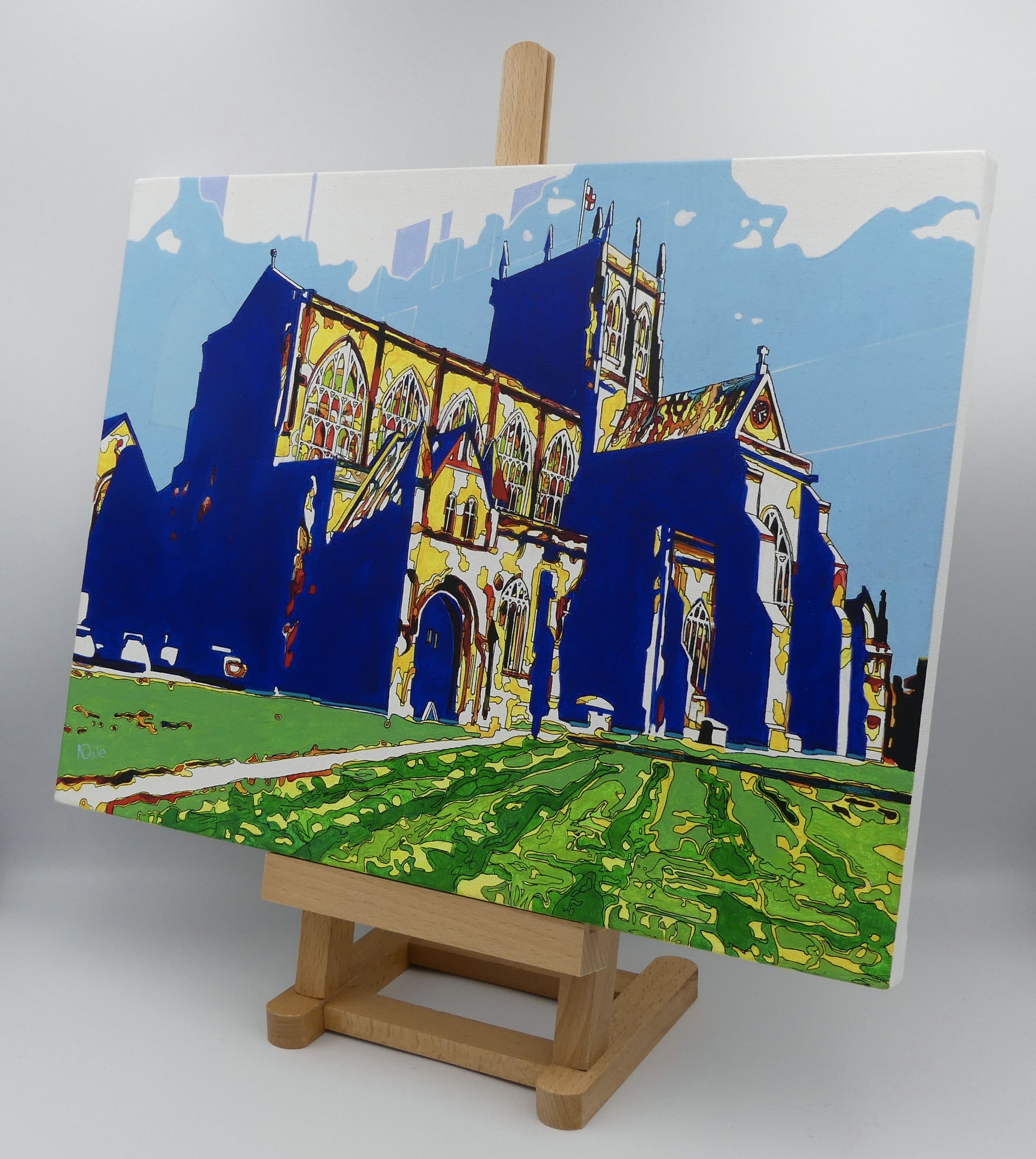 Image of the original painting 'Sherborne Abbey Radiant' by Nick Dale on a small easel. The painting depicts Sherborne Abbey in bright primary colours with strong shadows and a brightly lit south-facing aspect.