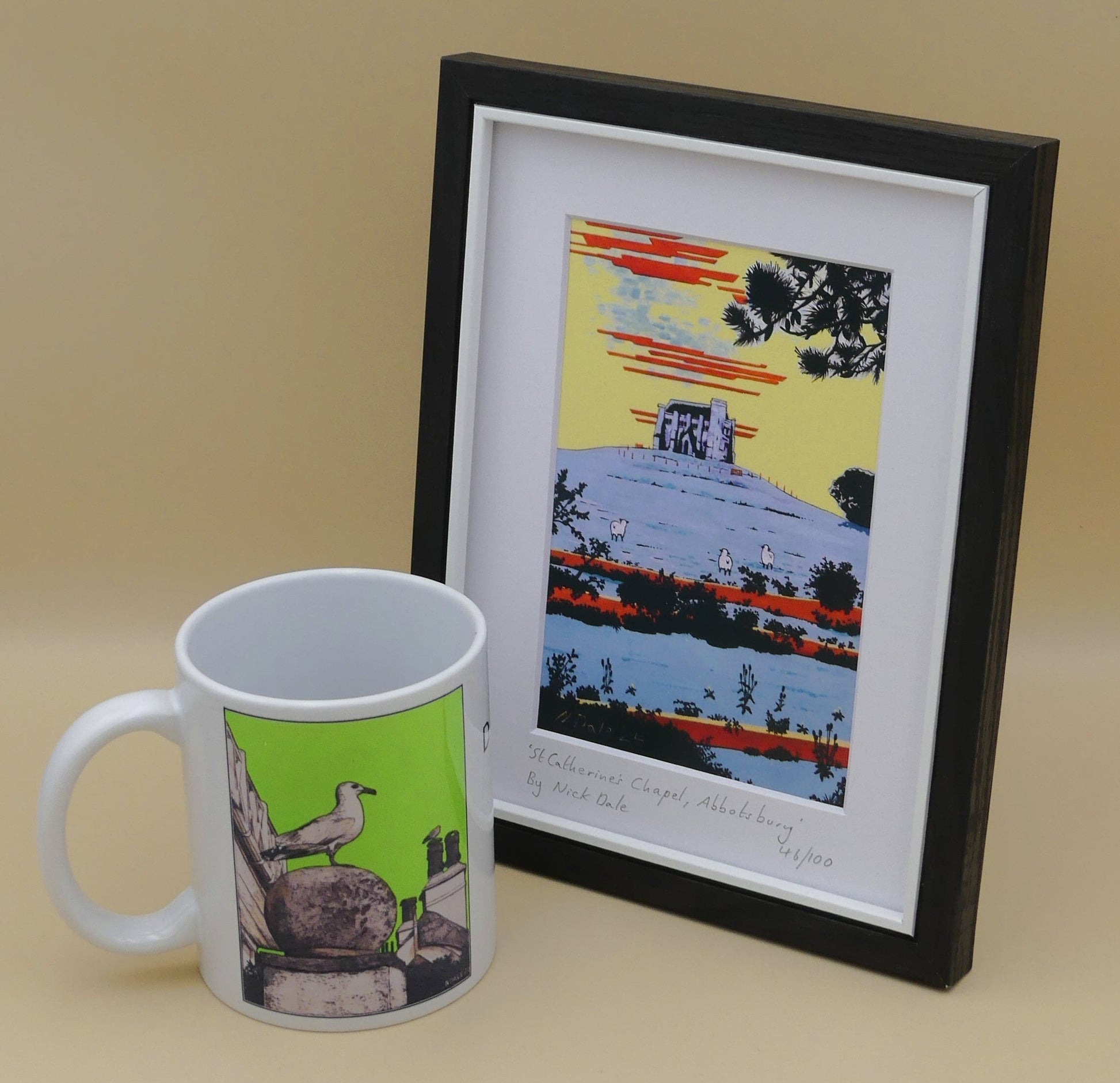 Image of Small Art Print featuring a copy of the painting 'St Catherine's Chapel, Abbotsbury' by Nick Dale. The print depicts the Medieval St Catherine's Chapel which is positioned overlooking the village of Abbotsbury.  The print is situated in a black frame next to a mug.