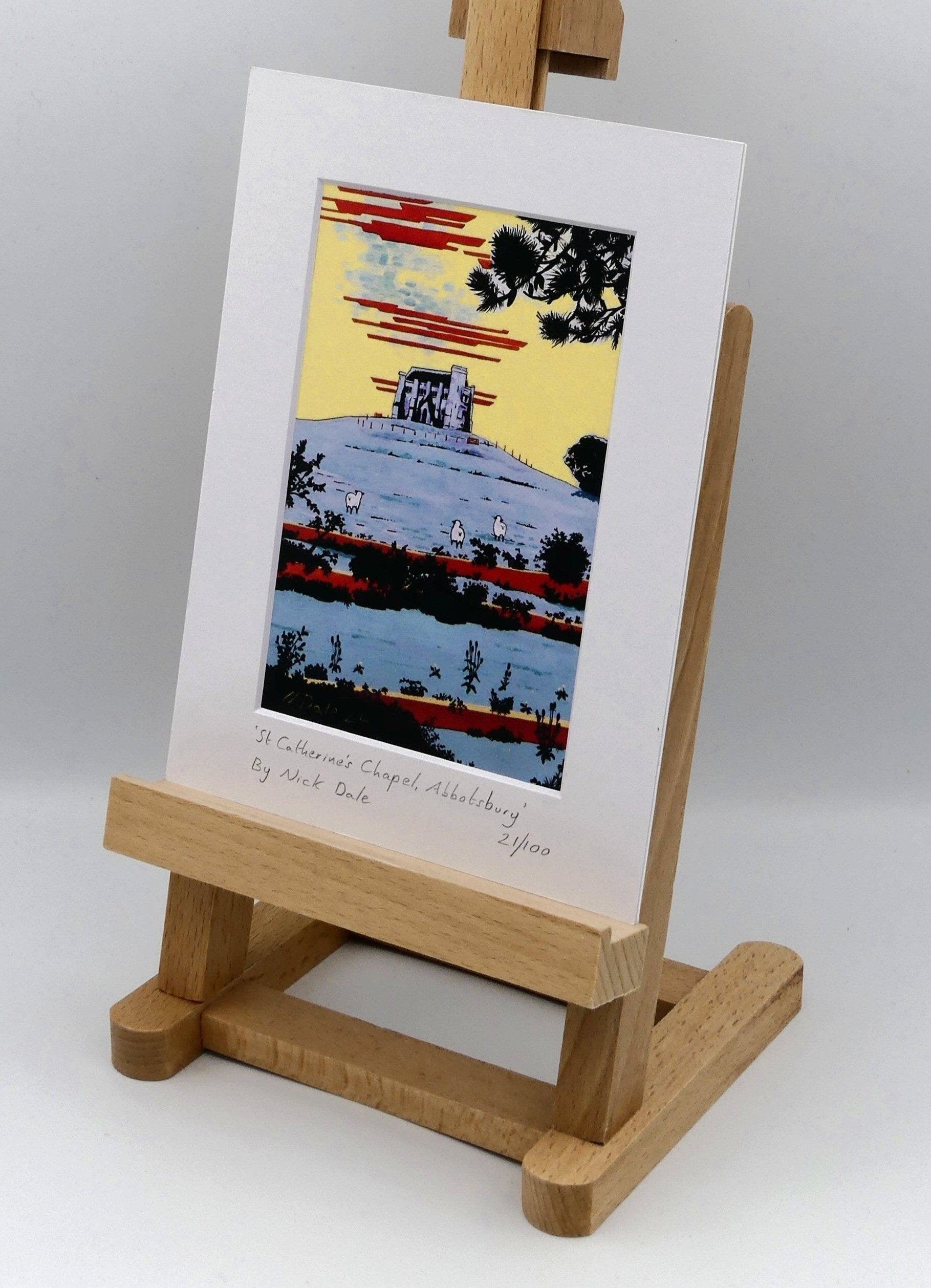 Image of Small Art Print featuring a copy of the painting 'St Catherine's Chapel, Abbotsbury' by Nick Dale. The print depicts the Medieval St Catherine's Chapel which is positioned overlooking the village of Abbotsbury. The print is situated on a small easel.