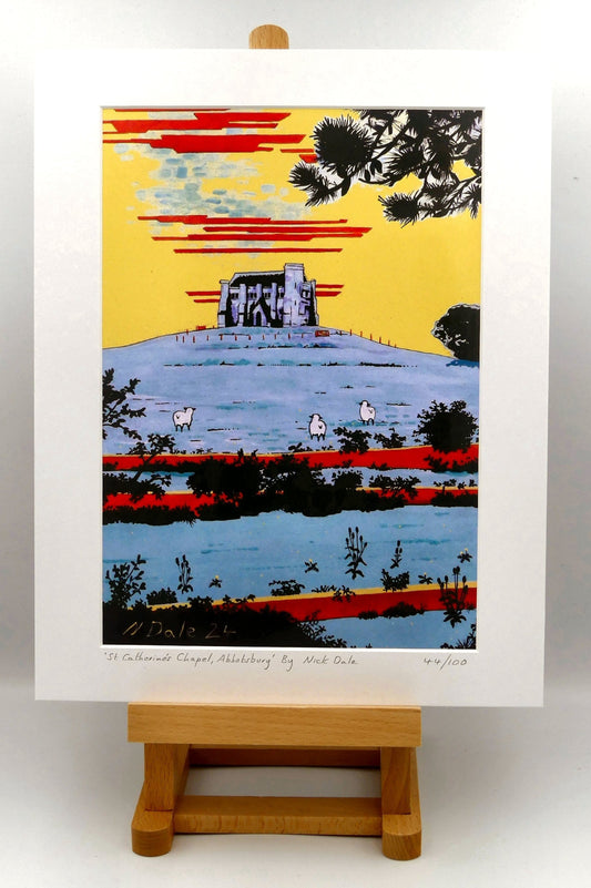 Image of a Medium Art Print (A4 size) featuring a copy of the painting 'St Catherine's Chapel, Abbotsbury' by Nick Dale. The print depicts the Medieval St Catherine's Chapel which is positioned overlooking the village of Abbotsbury. The print is situated on a small easel.
