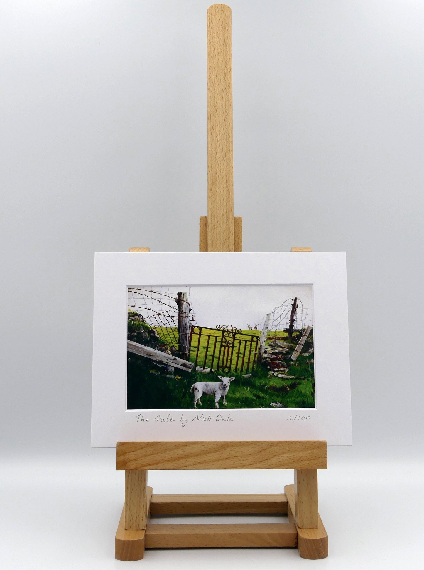 Image of a Small Art Print featuring a copy of the painting 'The Gate' by Nick Dale.The print depicts a lamb in front of an ornamental garden gate reused by a farmer somewhere in North Devon, probably to the south of Valley of Rocks, Lynton. The lamb was observed on Lundy Island, Devon. The print is situated on a small easel.