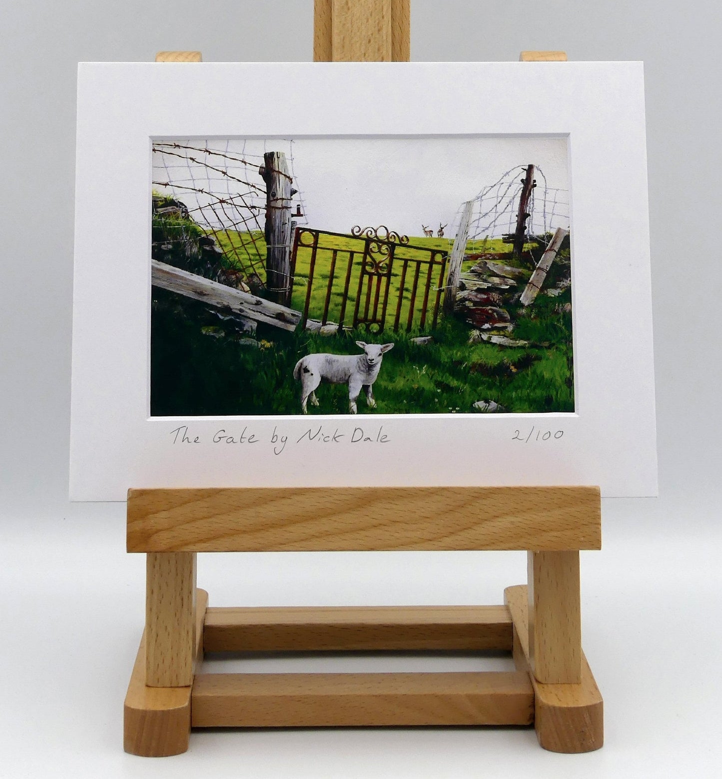 Image of a Small Art Print featuring a copy of the painting 'The Gate' by Nick Dale.The print depicts a lamb in front of an ornamental garden gate reused by a farmer somewhere in North Devon, probably to the south of Valley of Rocks, Lynton. The lamb was observed on Lundy Island, Devon. The print is situated on a small easel.
