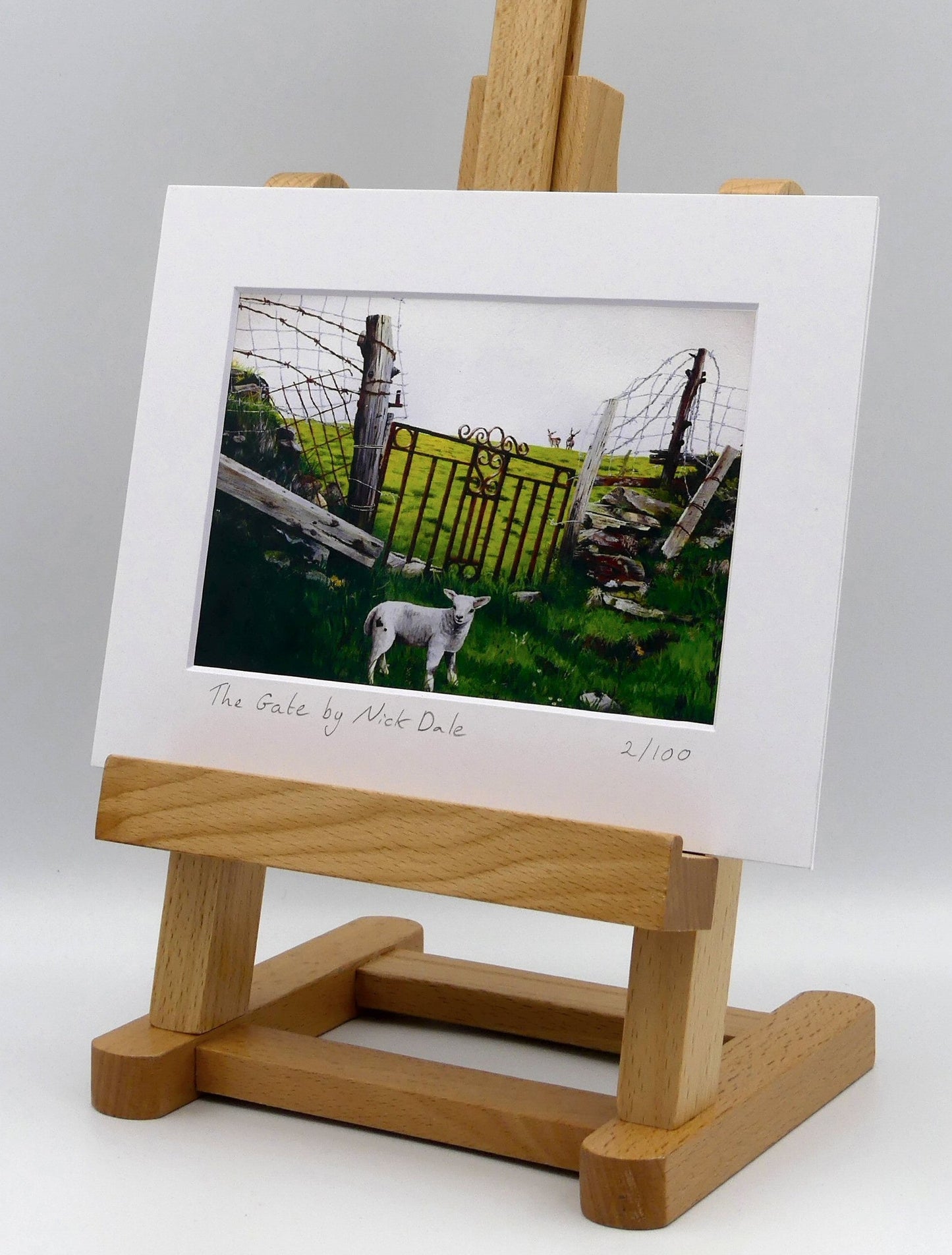 Image of a Small Art Print featuring a copy of the painting 'The Gate' by Nick Dale.The print depicts a lamb in front of an ornamental garden gate reused by a farmer somewhere in North Devon, probably to the south of Valley of Rocks, Lynton. The lamb was observed on Lundy Island, Devon. The print is situated on a small easel.