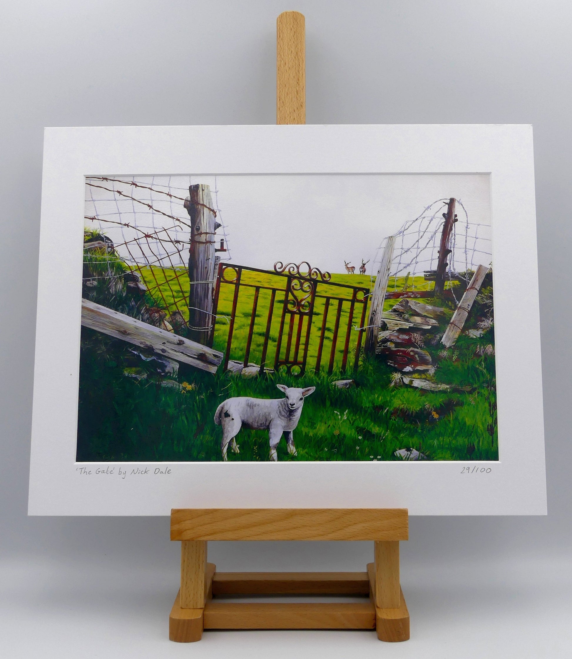 Image of a Medium Art Print featuring a copy of the painting 'The Gate' by Nick Dale. The print depicts a lamb in front of an ornamental garden gate reused by a farmer somewhere in North Devon, probably to the south of Valley of Rocks, Lynton. The lamb was observed on Lundy Island, Devon. The print is situated on a small easel.