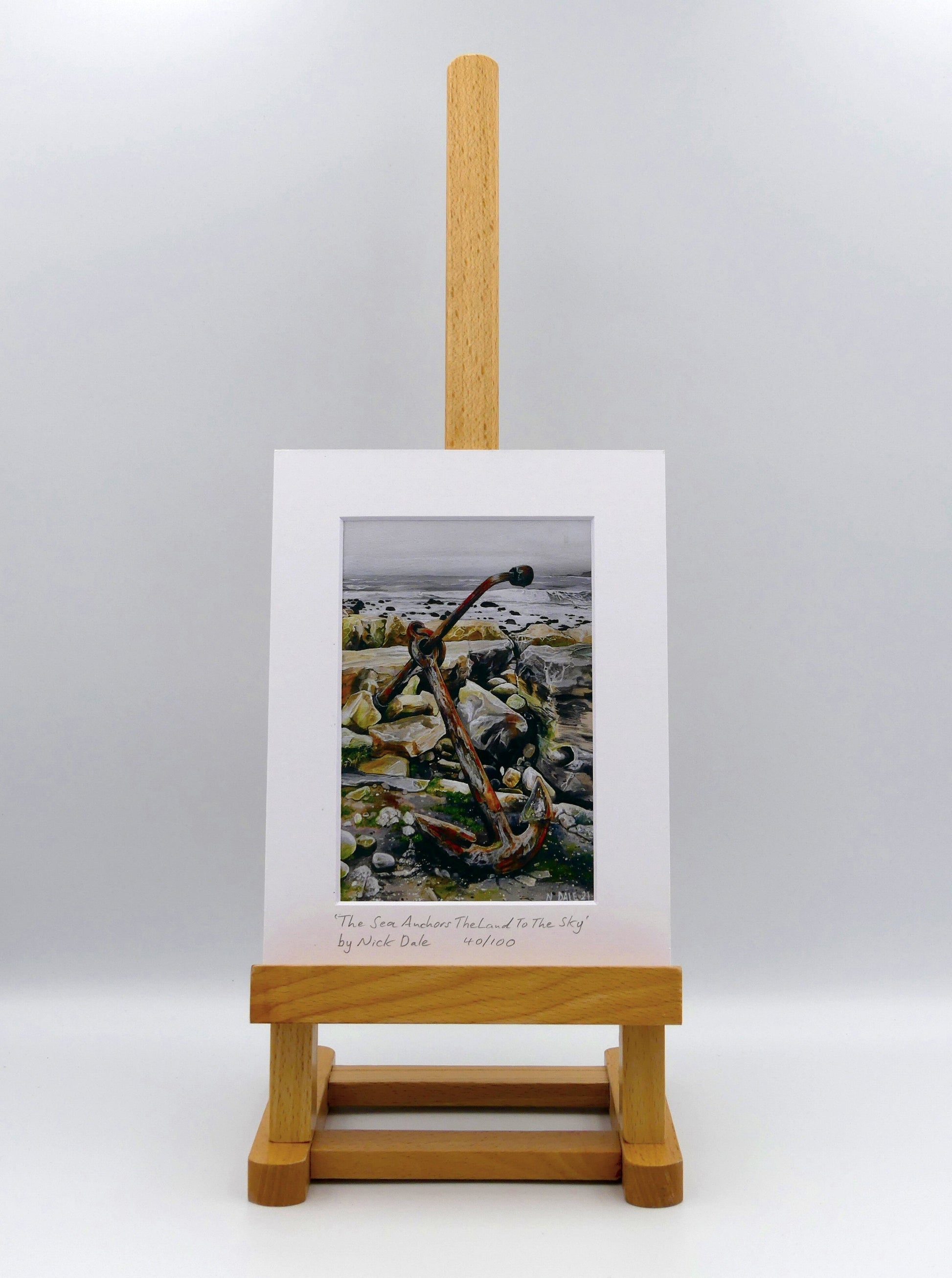 Image of a Small Art Print featuring a copy of the painting 'The Sea Anchors The Land To The Sky' by Nick Dale. The print depicts an old anchor lying at rest under a leaden sky upon the foreshore at Chapman's Pool, near Worth Matravers, Dorset. The print is situated on a small easel.