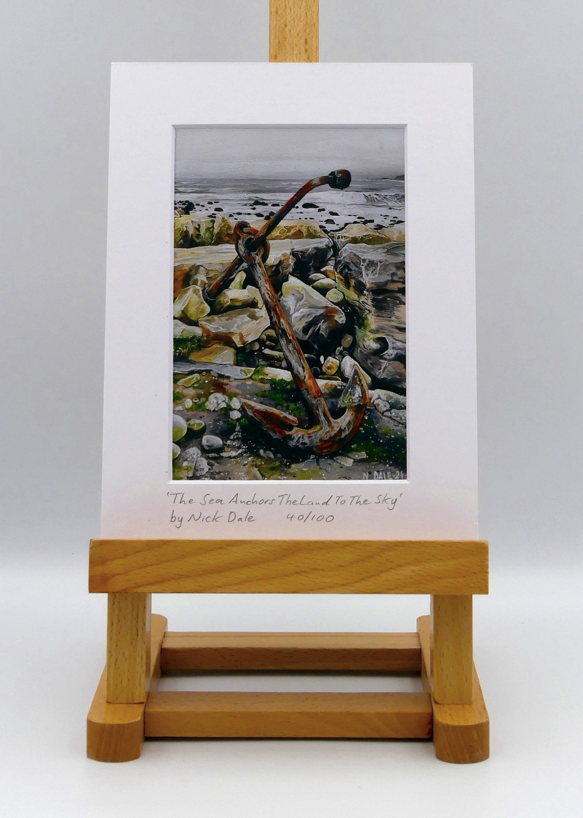 Image of a Small Art Print featuring a copy of the painting 'The Sea Anchors The Land To The Sky' by Nick Dale. The print depicts an old anchor lying at rest under a leaden sky upon the foreshore at Chapman's Pool, near Worth Matravers, Dorset. The print is situated on a small easel.