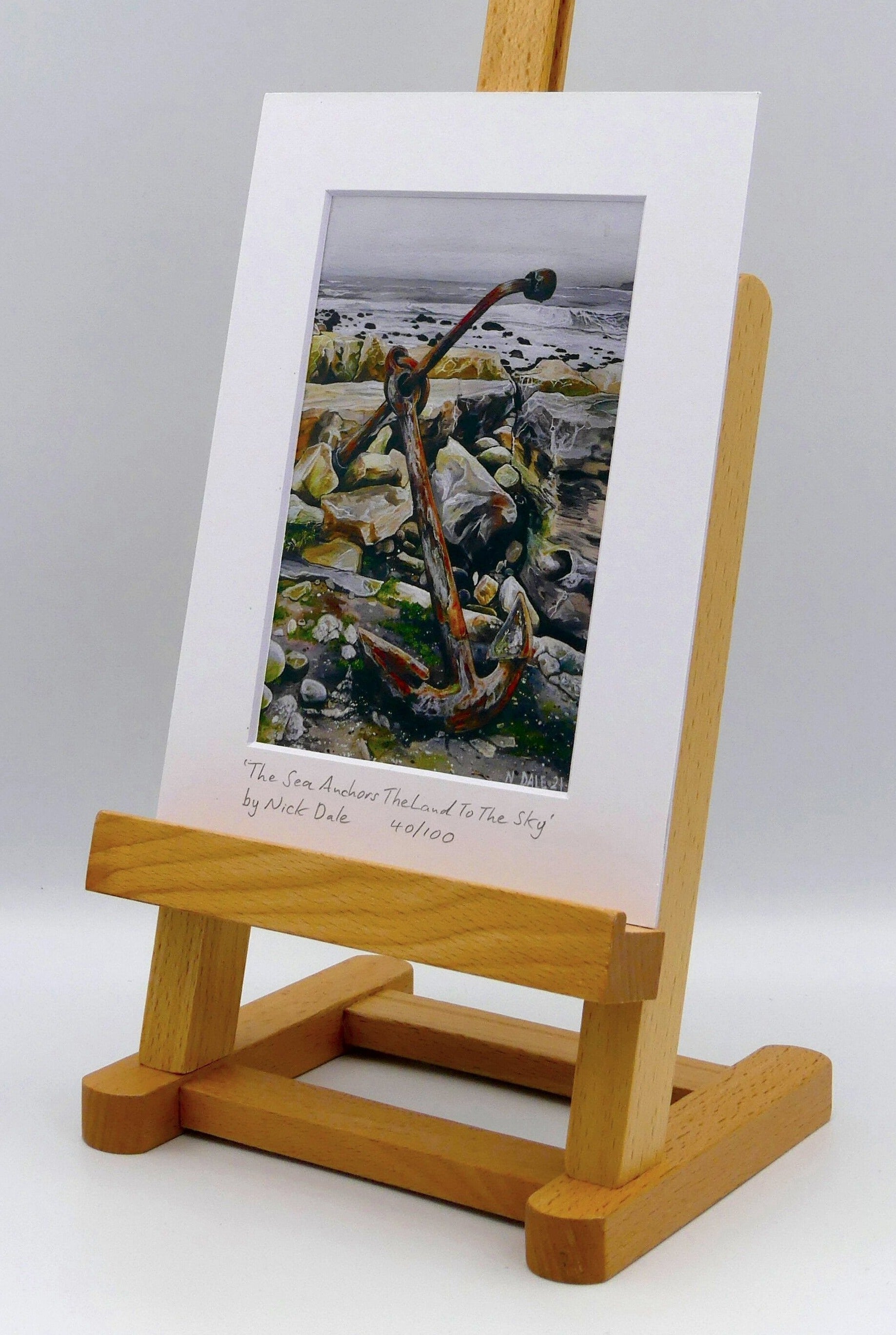 Image of a Small Art Print featuring a copy of the painting 'The Sea Anchors The Land To The Sky' by Nick Dale. The print depicts an old anchor lying at rest under a leaden sky upon the foreshore at Chapman's Pool, near Worth Matravers, Dorset. The print is situated on a small easel.