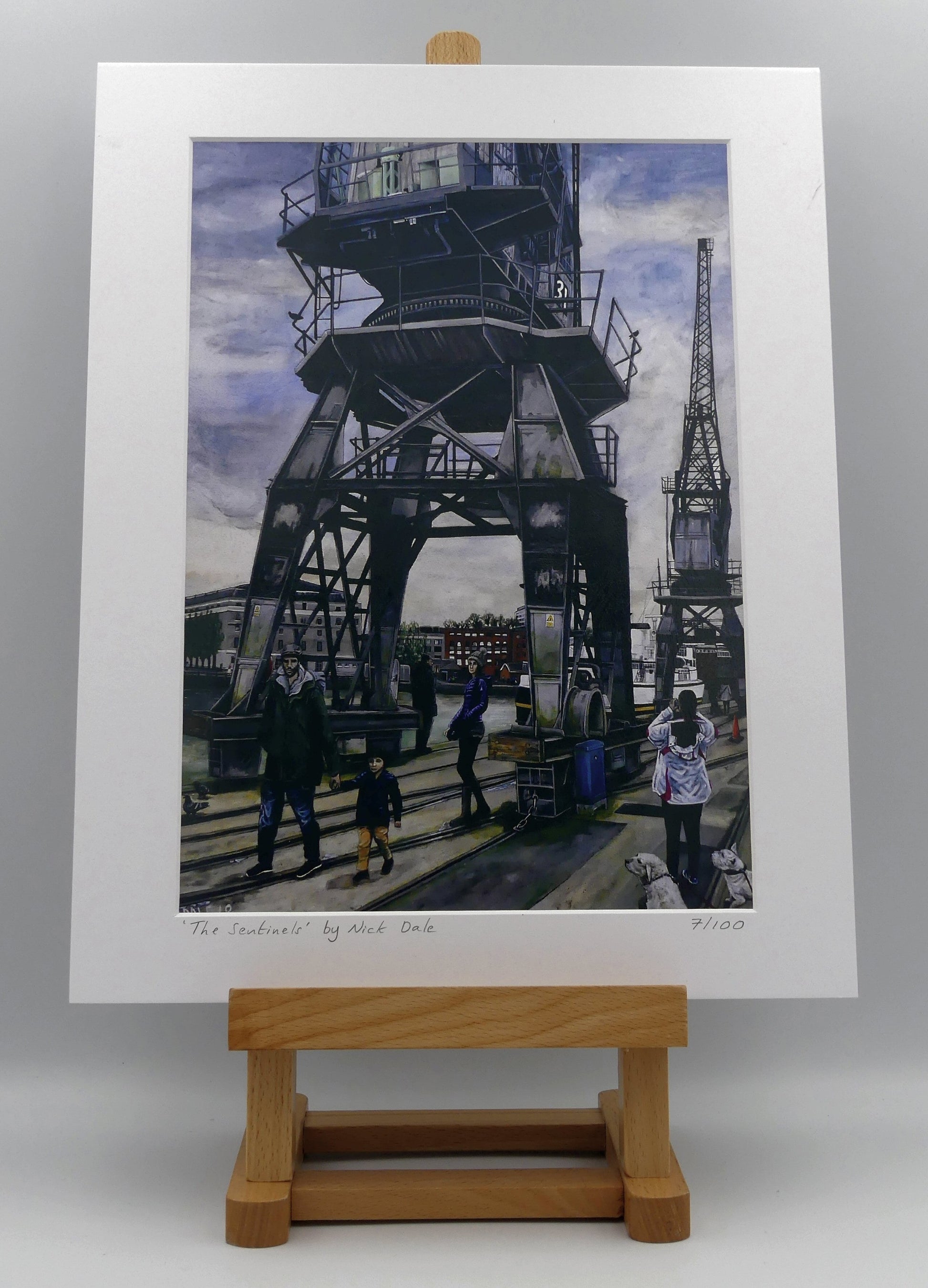 Image of a Medium Art Print featuring a copy of the painting 'The Sentinels' by Nick Dale. The print depicts the iconic tower cranes of Bristol Docks and the classic ship MV Balmoral beyond them. The print is situated on a small easel.