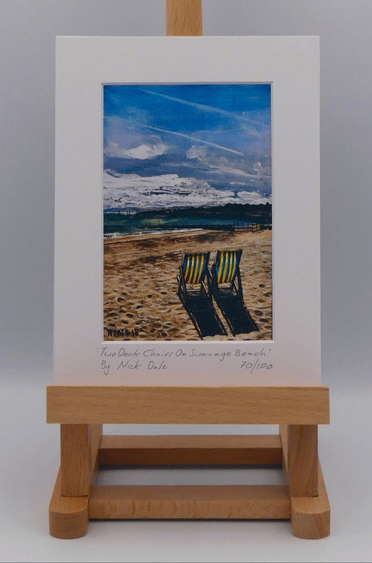 Image of a Small Art Print featuring a copy of the painting 'Two Deck Chairs On Swanage Beach' by Nick Dale. The print depicts two deck chairs overlooking the calm water from Swanage Beach (Dorset) towards Peveril Point. The print is situated on a small easel.