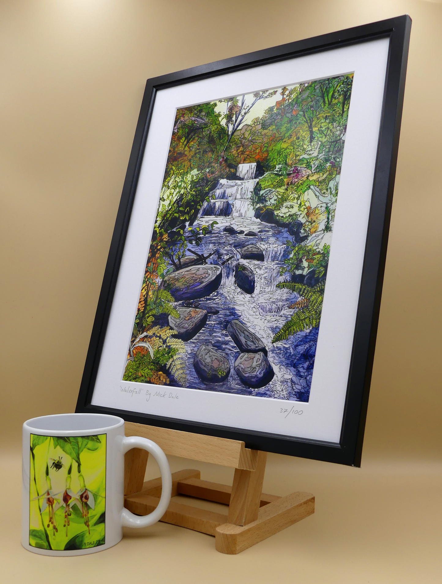 Image of a Medium Art Print featuring a copy of the painting 'Waterfall' by Nick Dale. The scene depicts the Hoar Oak Waterfall on the Hoar Oak Water moorland tributary of the East Lyn River at the famous National Trust site of Watersmeet House, Lynmouth, Devon. The print is situated on a small easel in a black frame next to a mug.