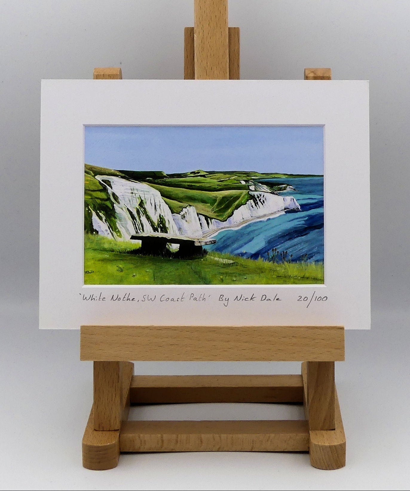 Image of a Small Art Print featuring a copy of the painting 'White Nothe, SW Coast Path' by Nick Dale. The print depicts a view along the Jurassic Coast from the White Nothe chalk headland east of Ringstead Bay. The view looks east over Bat's Head, Swyre Head and Durdle Door to St Oswald's Bay & beyond.  The print is situated on a small easel.