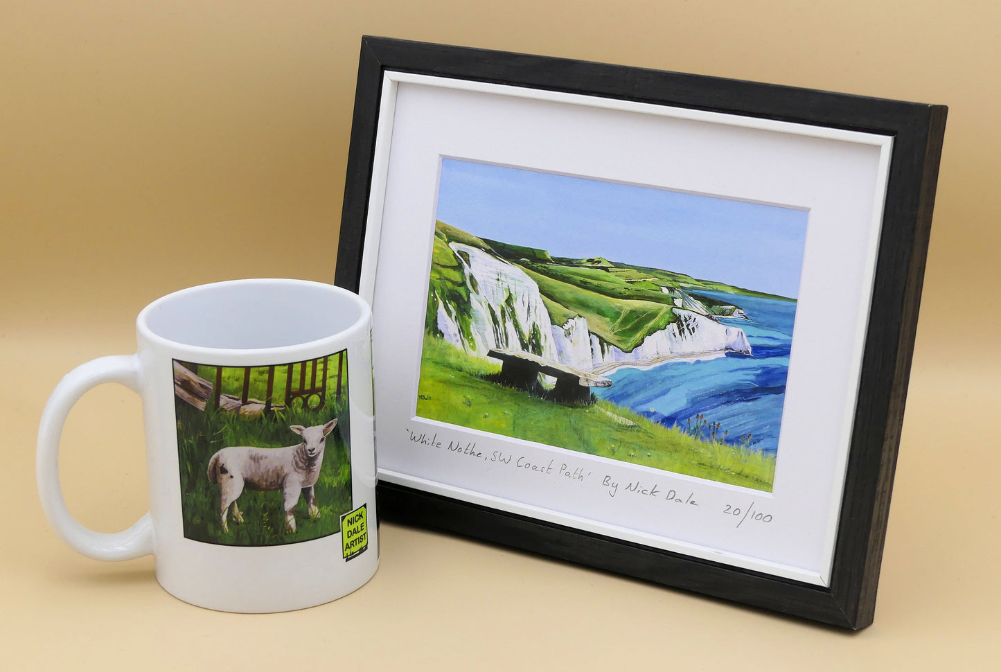 Image of a Small Art Print featuring a copy of the painting 'White Nothe, SW Coast Path' by Nick Dale. The print depicts a view along the Jurassic Coast from the White Nothe chalk headland east of Ringstead Bay. The view looks east over Bat's Head, Swyre Head and Durdle Door to St Oswald's Bay & beyond. The print is situated in a black frame next to a mug.