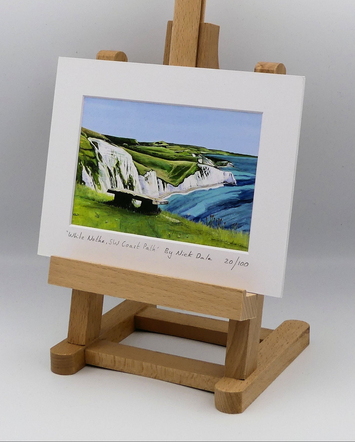 Image of a Small Art Print featuring a copy of the painting 'White Nothe, SW Coast Path' by Nick Dale. The print depicts a view along the Jurassic Coast from the White Nothe chalk headland east of Ringstead Bay. The view looks east over Bat's Head, Swyre Head and Durdle Door to St Oswald's Bay & beyond. The print is situated on a small easel.