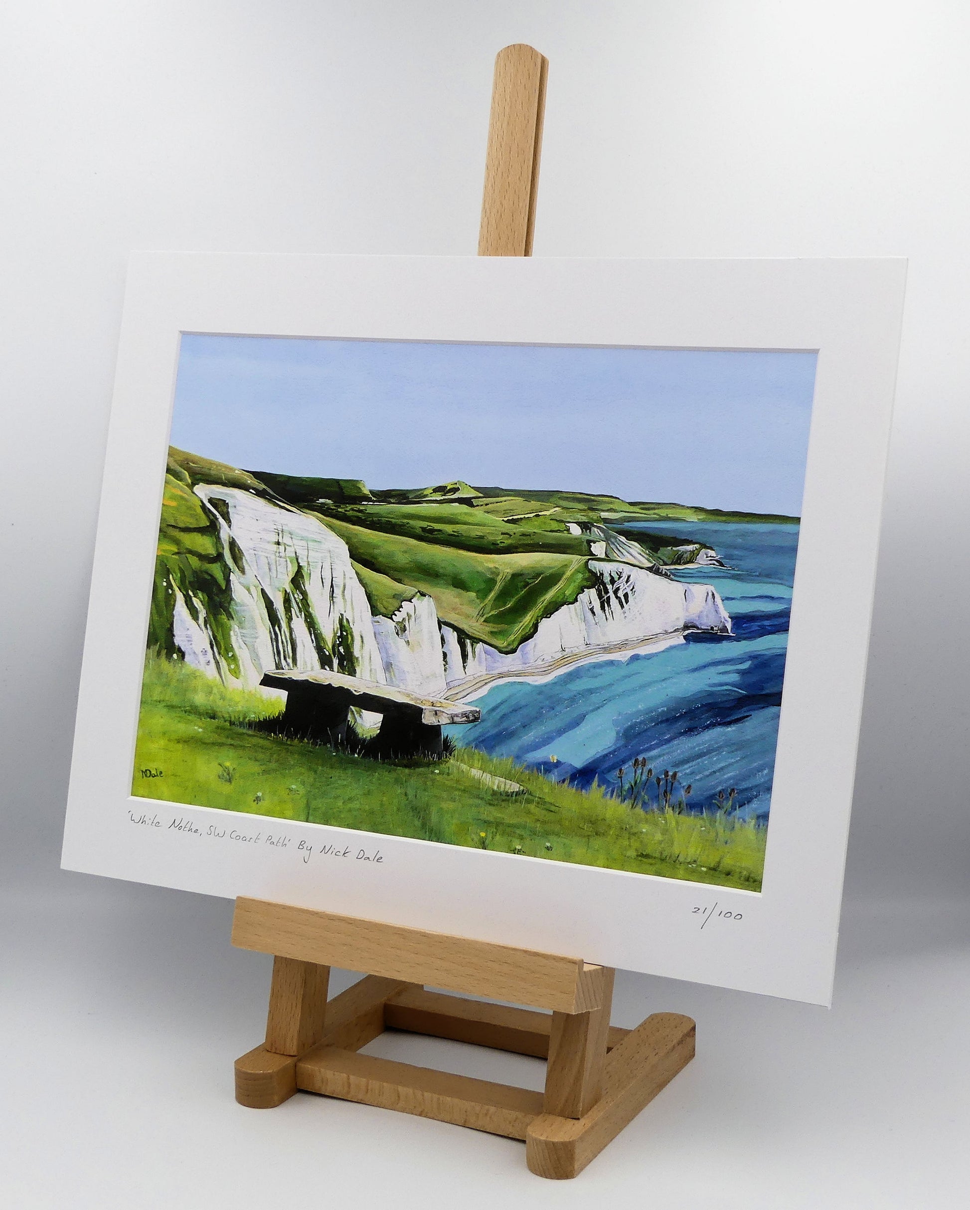 Image of a Medium Art Print featuring a copy of the painting 'White Nothe, SW Coast Path' by Nick Dale. The print depicts a view along the Jurassic Coast from the White Nothe chalk headland east of Ringstead Bay. The view looks east over Bat's Head, Swyre Head and Durdle Door to St Oswald's Bay & beyond. The print is situated on a small easel.