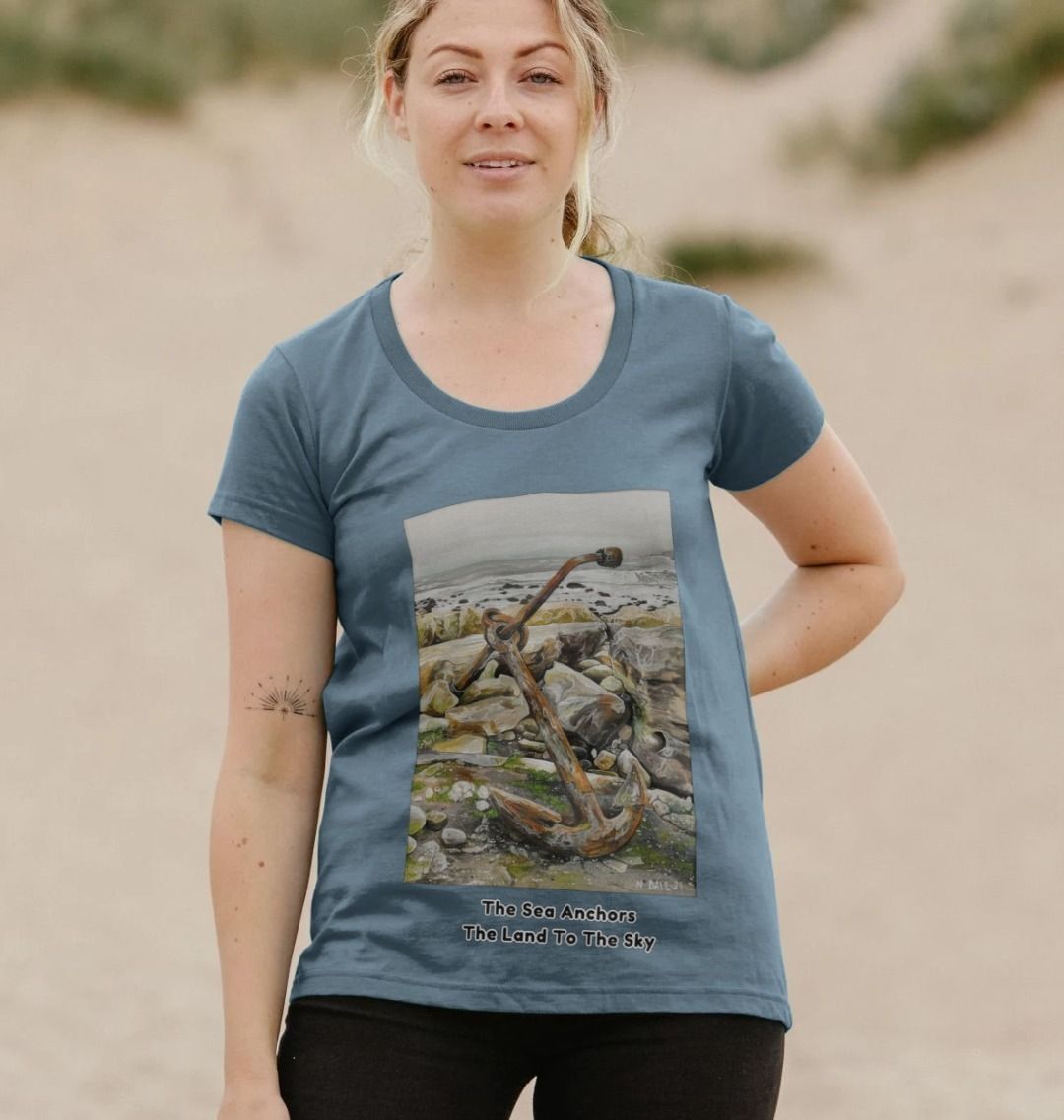 Image of a female model wearing a Stone Blue Women's Scoop Neck T-shirt featuring a copy of the painting 'The Sea Anchors The Land To The Sky' by Nick Dale, with the words 'The Sea Anchors The Land To The Sky' written beneath it. The T-shirt depicts an old anchor lying at rest under a leaden sky upon the foreshore at Chapman's Pool, near Worth Matravers, Dorset.