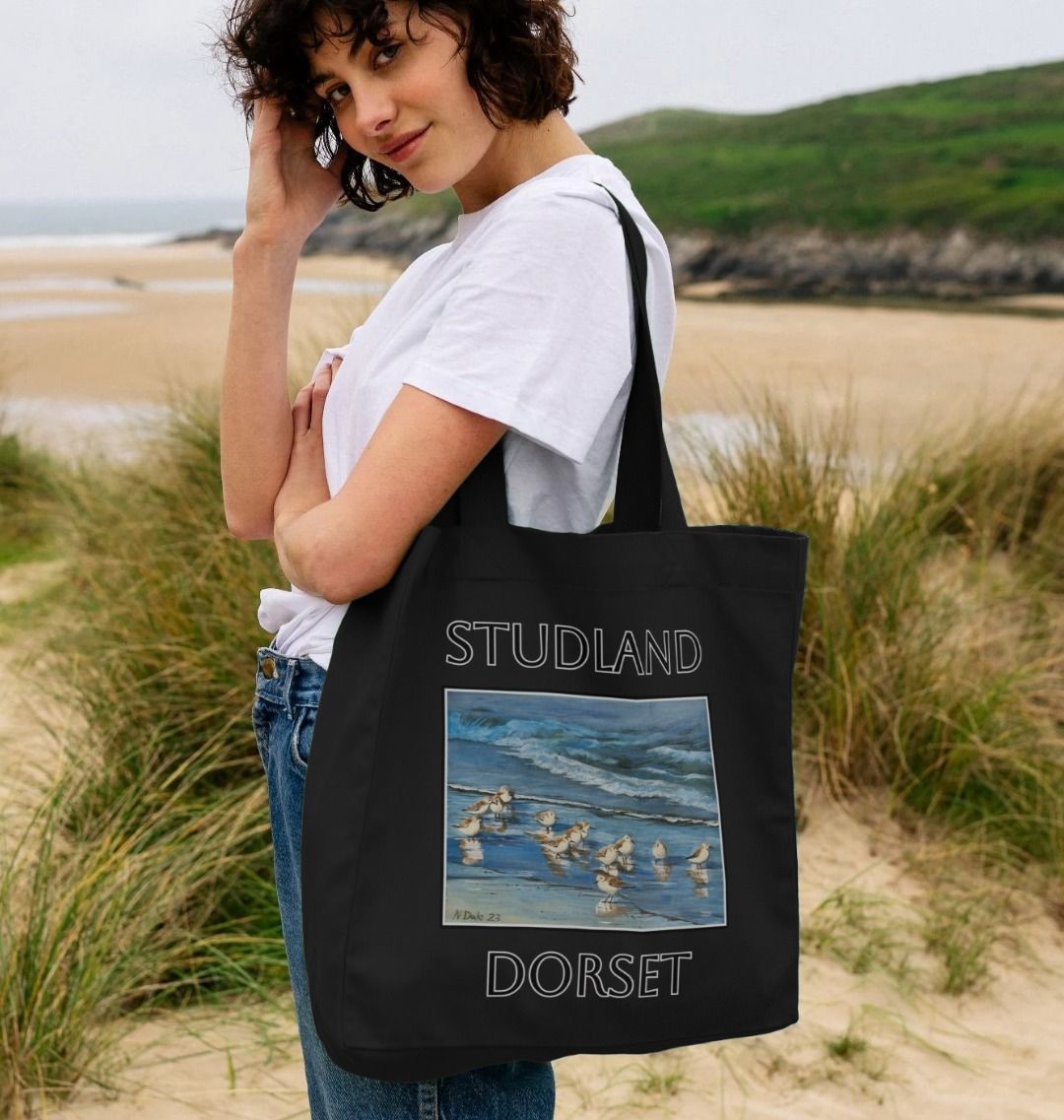 Image of a female model carrying a Black Shopper Tote Bag featuring a copy of the painting 'Studland Misty Morning' by Nick Dale. The bag depicts Dunlins on Studland Beach (Dorset) on a crisp and misty morning.