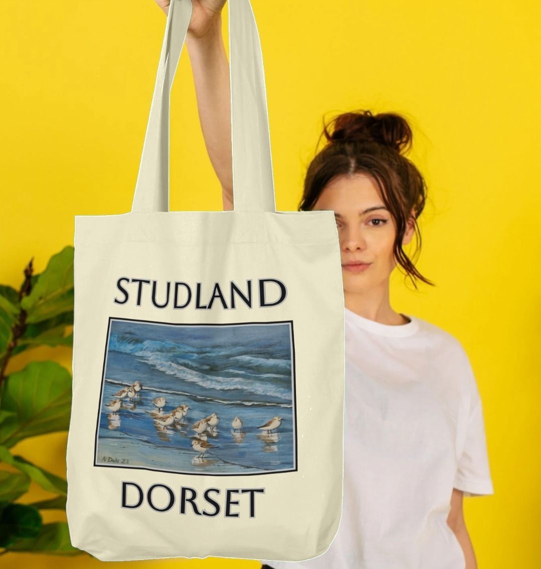 Image of a female model holding a Natural Tote Bag featuring a copy of the painting 'Studland Misty Morning' by Nick Dale. The bag depicts Dunlins on Studland Beach (Dorset) on a crisp and misty morning.