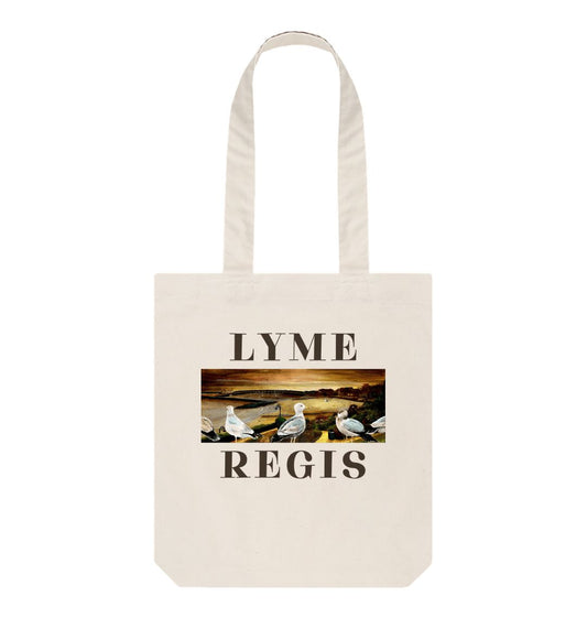 Image of a Natural Tote Bag featuring a copy of the painting 'The Flock Of Lyme Regis' by Nick Dale, with the word 'Lyme' written above it and the word 'Regis' written below it. The bag depicts a sunset view over the town and seafront, including the harbour and cobb at Lyme Regis, Dorset, from Langmoor Gardens.