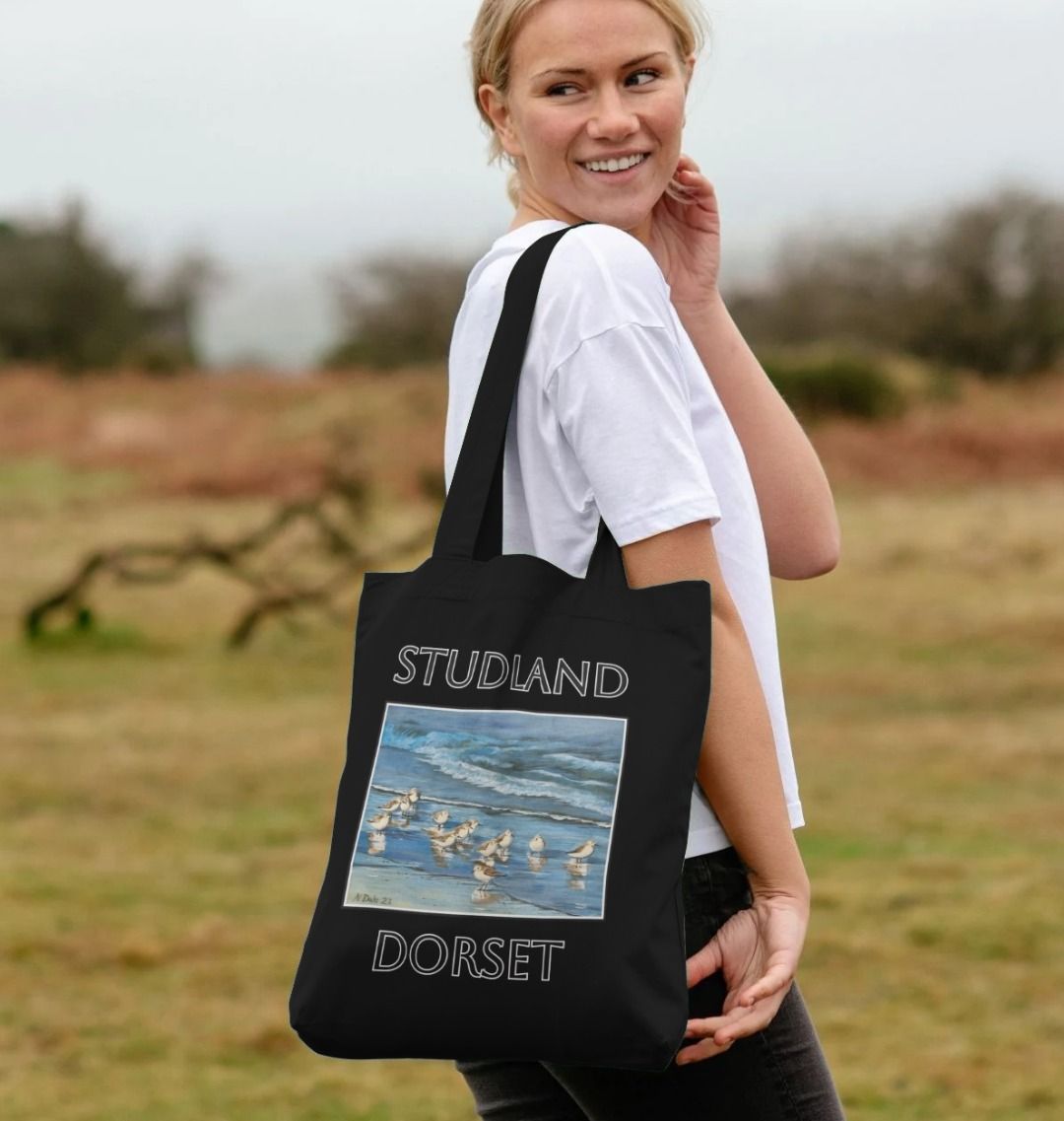 Image of a female model carrying a Black Tote Bag featuring a copy of the painting 'Studland Misty Morning' by Nick Dale. The bag depicts Dunlins on Studland Beach (Dorset) on a crisp and misty morning.