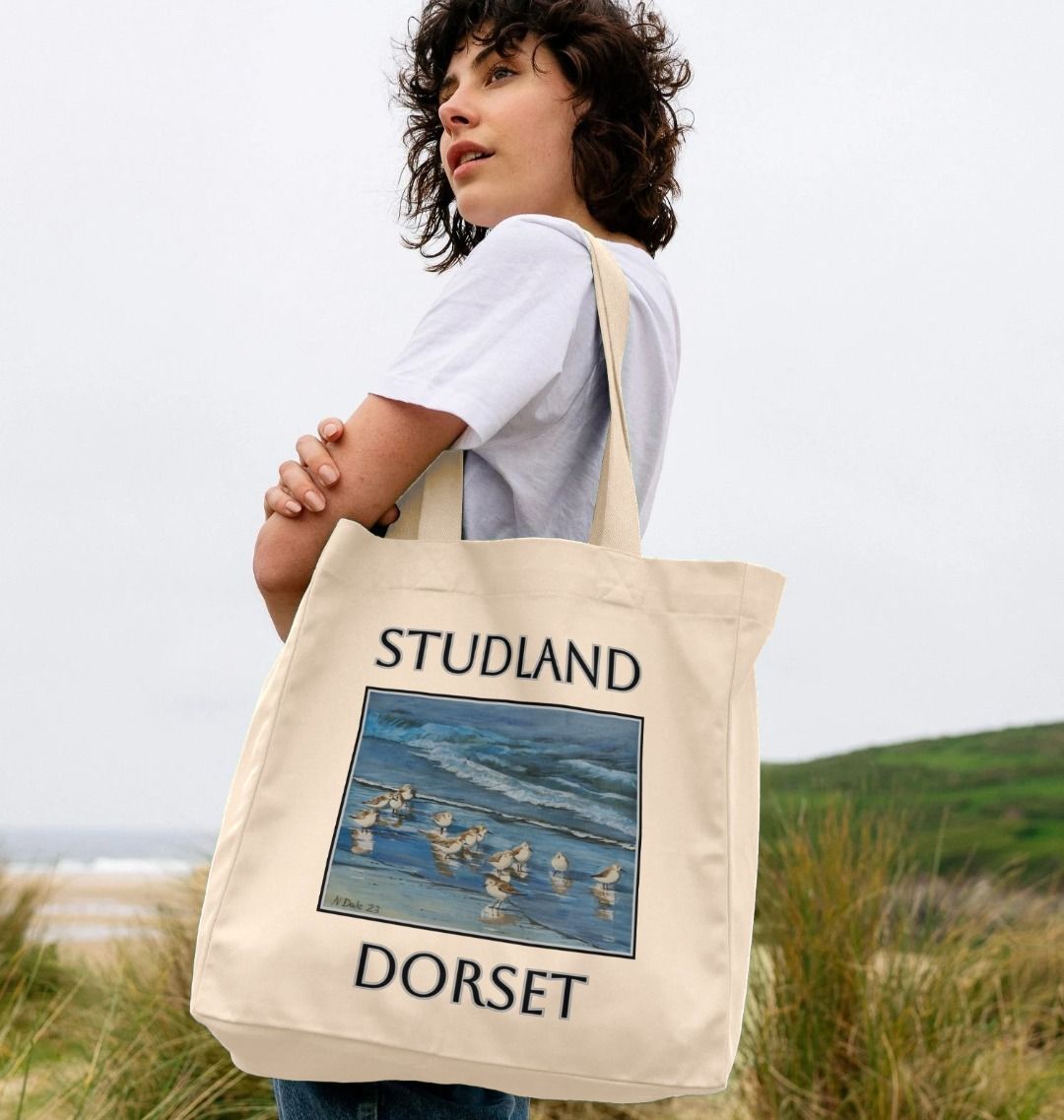 Image of a female model carrying a Natural Shopper Tote Bag featuring a copy of the painting 'Studland Misty Morning' by Nick Dale. The bag depicts Dunlins on Studland Beach (Dorset) on a crisp and misty morning.