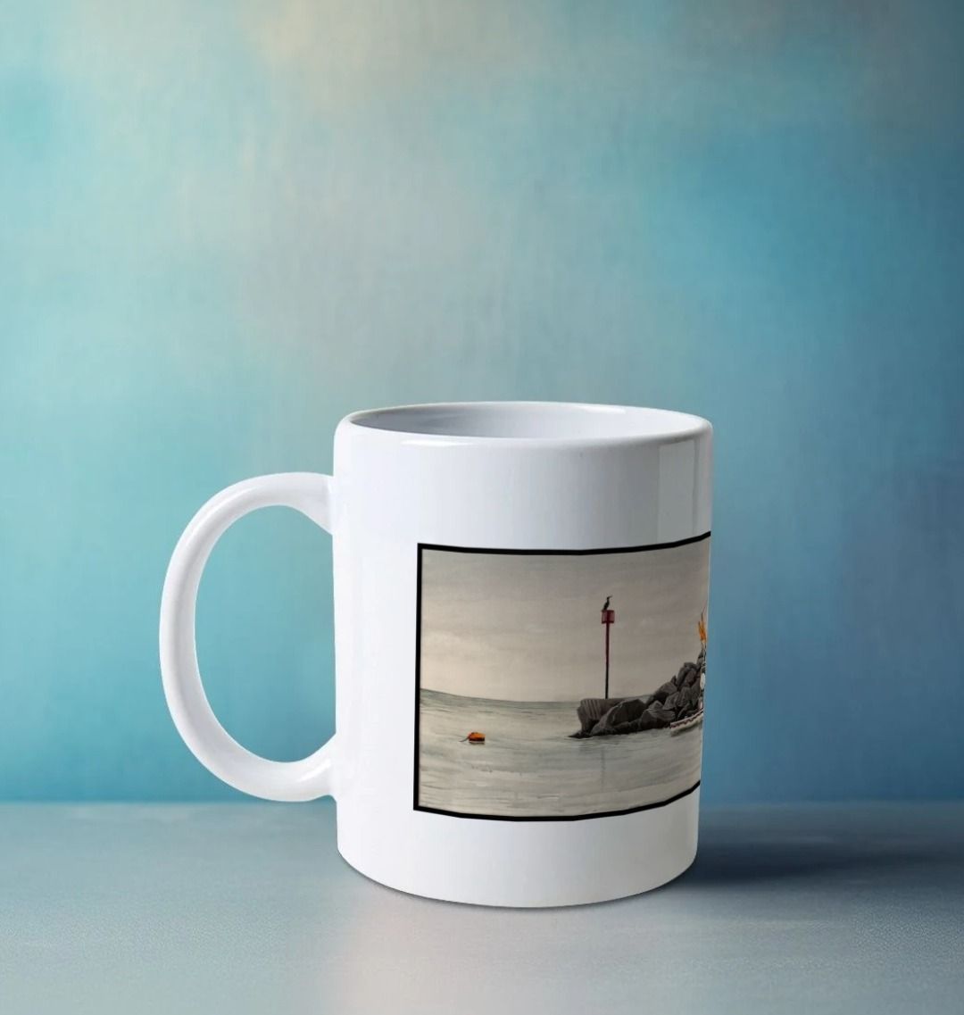 Image of a White Mug on a white table featuring a copy of the painting 'End Of The Line' by Nick Dale. The handle is orientated to the left. The mug depicts a scene where, as the fisherman prepares his catch for unloading at Lyme Regis, the birds line up on the breakwater and patiently await their turn to feed.