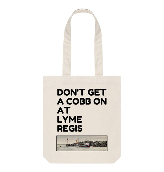 Image of a Natural Tote Bag featuring a copy of the painting 'End Of The Line' by Nick Dale with the slogan 'Don't Get A Cobb On At Lyme Regis' written above it. The bag depicts a fisherman preparing his catch for unloading at Lyme Regis as the birds line up on the breakwater and patiently await their turn to feed.
