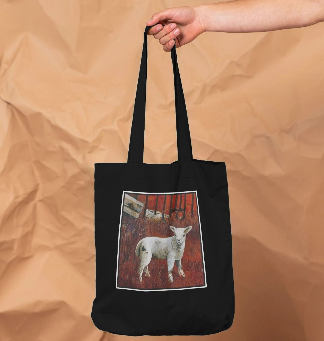 Image of a female model holding a Black Tote Bag featuring a modified copy of a detail from the painting 'The Gate' by Nick Dale. The bag depicts a lamb in front of an ornamental garden gate reused by a farmer somewhere in North Devon, probably to the south of Valley of Rocks, Lynton. The lamb was observed on Lundy Island, Devon.