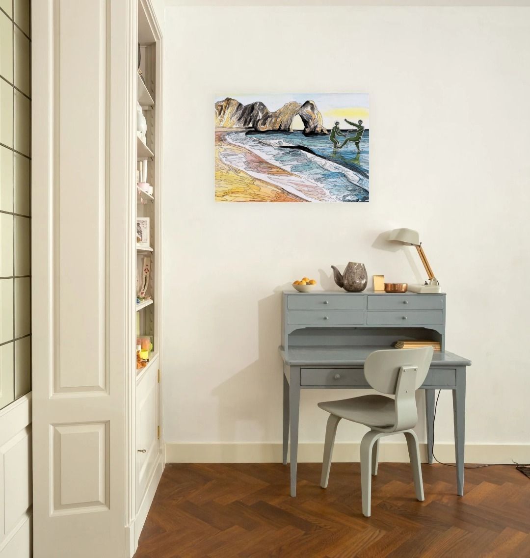 Image of a Large Art Print featuring a copy of the painting 'Mr & Mrs Cerne Abbas Giant Cavorting At Durdle Door' by Nick Dale; as displayed on a wall above a desk. The scene imagines the future Mr & Mrs Cerne Abbas Giant's first date at Durdle Door; where they cavort in the water in front of the famous Dorset landmark.