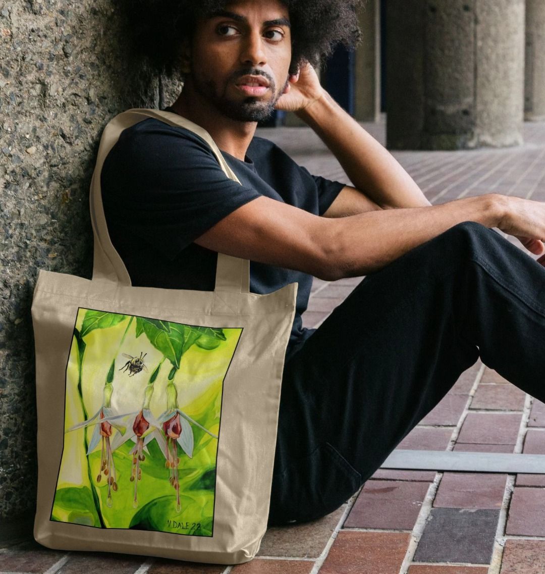Image of a male model carrying a Natural Tote Bag featuring a copy of the painting 'The Three Muses' by Nick Dale. The bag depicts a close-up view of a bee approaching its prize. But which will it choose?