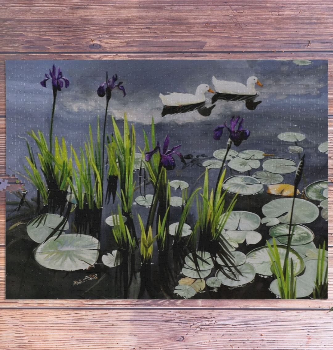 Image of a 1000 Piece Jigsaw Puzzle featuring a copy of the painting 'Dark Waters' by Nick Dale. As displayed partially completed on a wooden table. The jigsaw depicts lily pads, irises and ducks on a pond at Knightshayes Court, Devon.