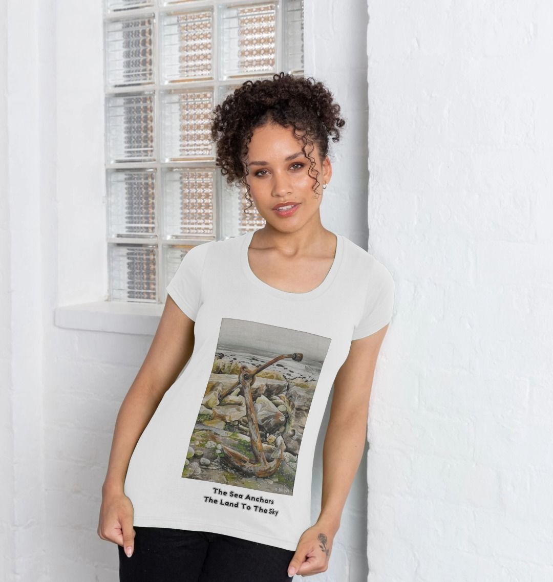 Image of a female model wearing a White Women's Scoop Neck T-shirt featuring a copy of the painting 'The Sea Anchors The Land To The Sky' by Nick Dale, with the words 'The Sea Anchors The Land To The Sky' written beneath it. The T-shirt depicts an old anchor lying at rest under a leaden sky upon the foreshore at Chapman's Pool, near Worth Matravers, Dorset.