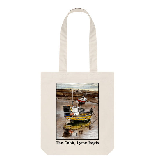 Image of a Natural Tote Bag featuring a copy of the painting 'Lyme Regis at Low Tide' by Nick Dale, with the words 'The Cobb, Lyme Regis' written beneath it. The bag depicts a sunset where the fishing vessels rest on the floor of Lyme Regis harbour whilst the tourists enjoy the view from the Cobb.