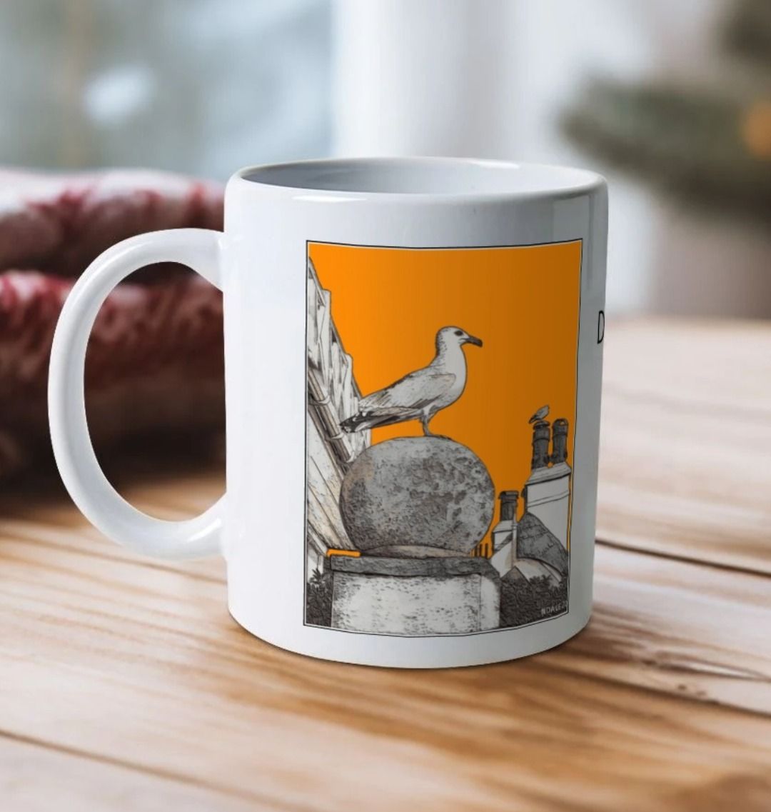 Image of a White Mug on a wooden table featuring a modified copy of the painting 'A View Of The Sea At Lyme Regis' by Nick Dale - this being the 'Orange' version. The handle is orientated to the left. The mug depicts a gull and buildings along Marine Parade, Lyme Regis.
