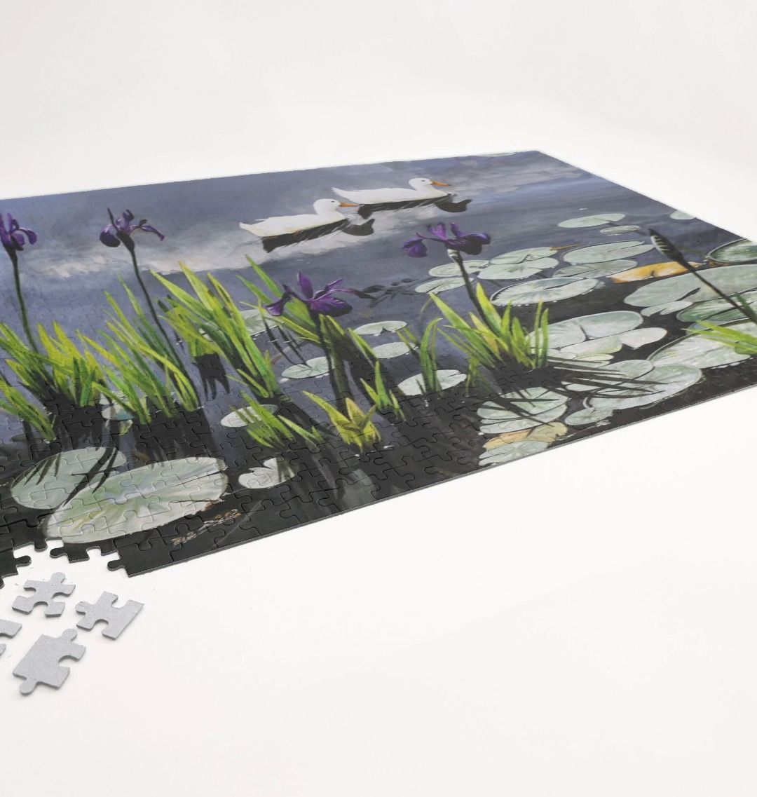 Image of a 1000 Piece Jigsaw Puzzle featuring a copy of the painting 'Dark Waters' by Nick Dale. As displayed partially completed on a white surface. The jigsaw depicts lily pads, irises and ducks on a pond at Knightshayes Court, Devon.