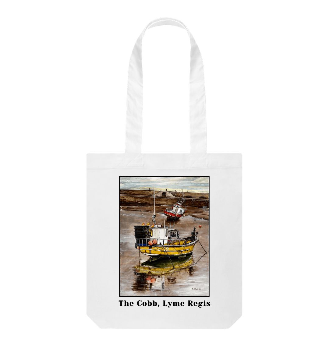 Image of a White Tote Bag featuring a copy of the painting 'Lyme Regis at Low Tide' by Nick Dale, with the words 'The Cobb, Lyme Regis' written beneath it. The bag depicts a sunset where the fishing vessels rest on the floor of Lyme Regis harbour whilst the tourists enjoy the view from the Cobb.