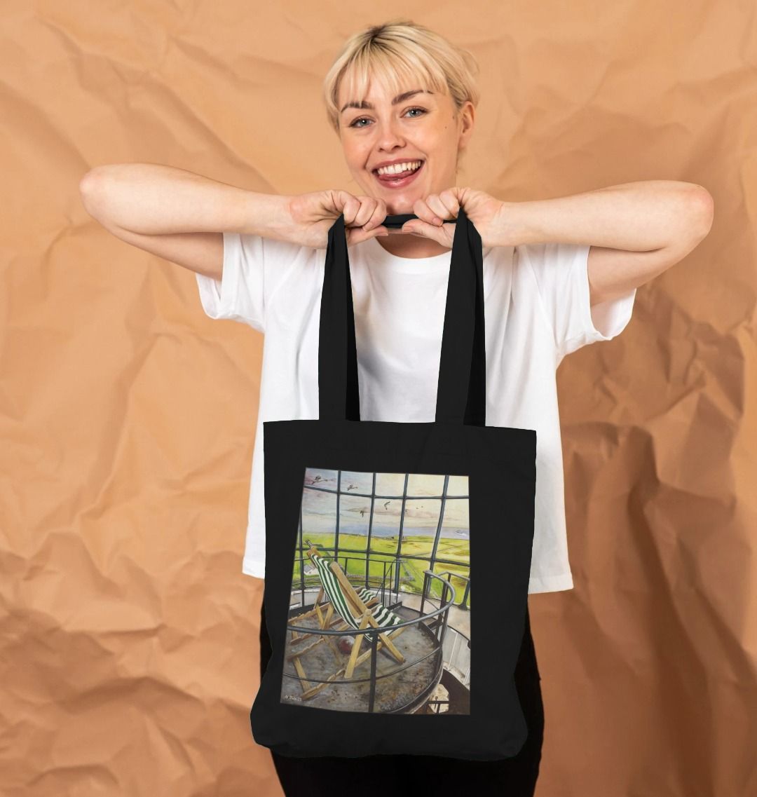 Image of a female model holding a Black Tote Bag featuring a copy of the painting 'Let's Be Together Alone' by Nick Dale. The bag depicts the view from the lantern room of the Old Light lighthouse on Beacon Hill, on the island of Lundy, Devon.