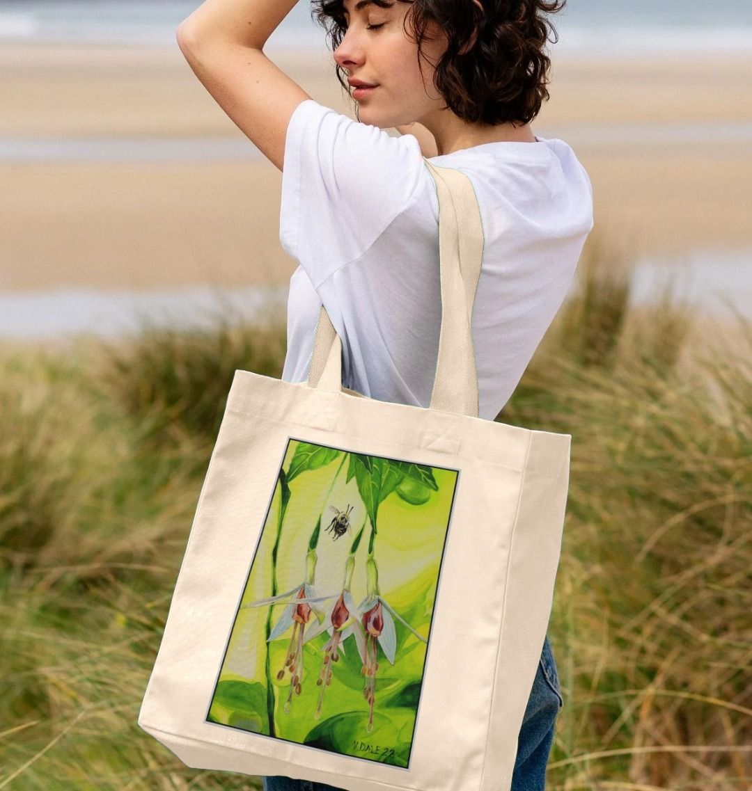 Image of a female model carrying a Natural Shopper Tote Bag featuring a copy of the painting 'The Three Muses' by Nick Dale. The bag depicts a close-up view of a bee approaching its prize. But which will it choose?
