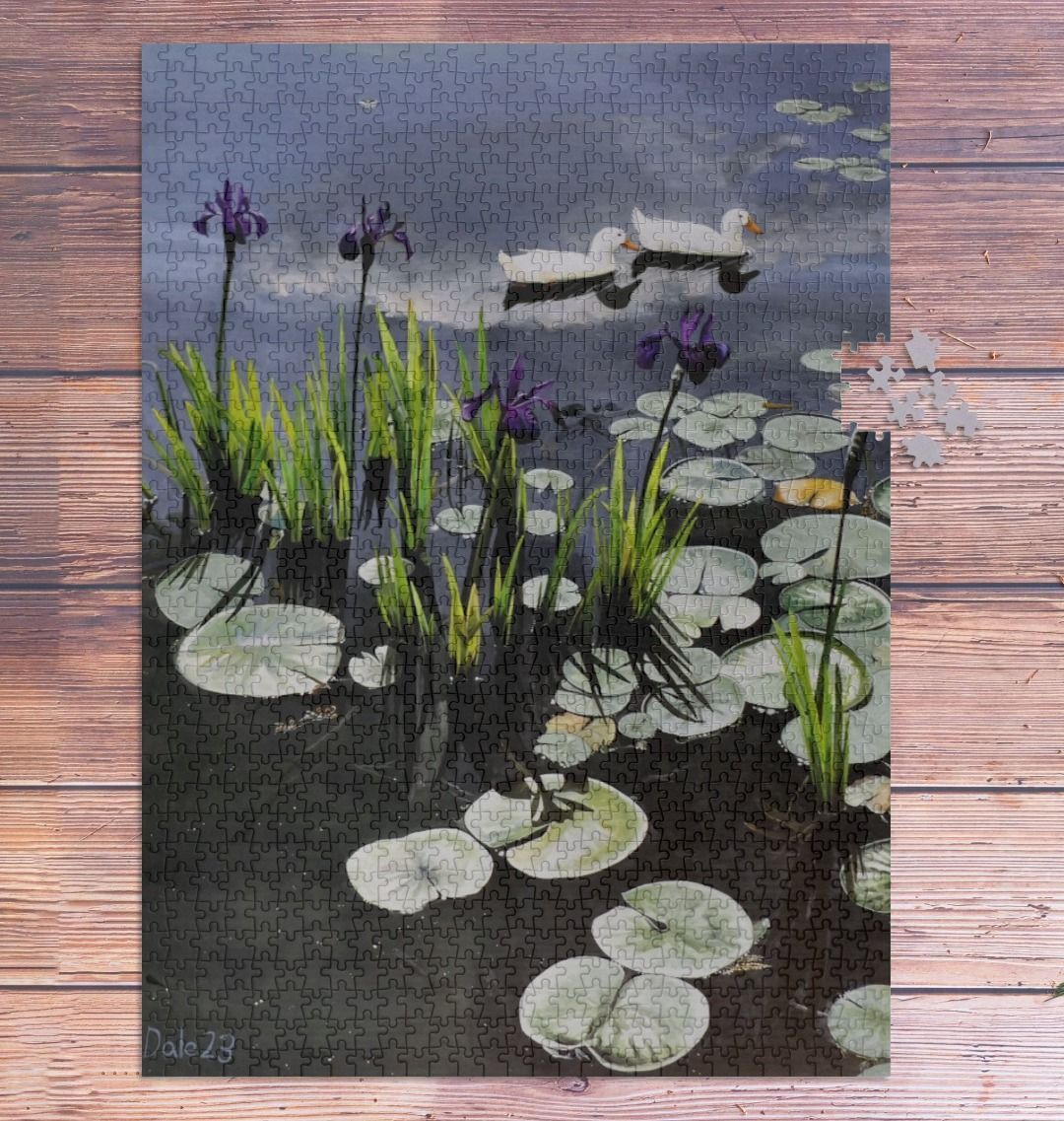 Image of a 1000 Piece Jigsaw Puzzle featuring a copy of the painting 'Dark Waters' by Nick Dale. As displayed partially completed on a wooden table. The jigsaw depicts lily pads, irises and ducks on a pond at Knightshayes Court, Devon.